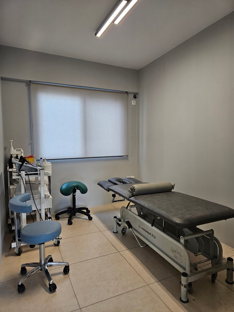 Ιατρικό εξεταστήριο με κρεβάτι θεραπείας, μπλε σκαμπό και καρότσι εξοπλισμού